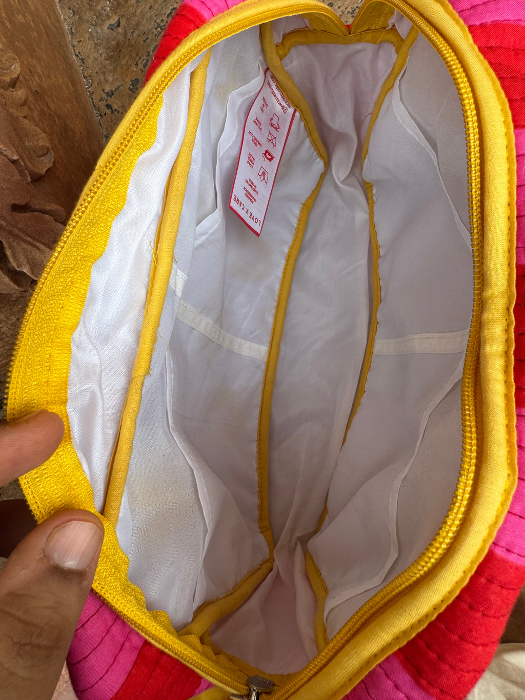 Close-up of the open interior of a zippered bag or pouch, showing an ultra-soft waterproof lining with very handy pockets for your essentials. A hand is holding the left edge of the opening.